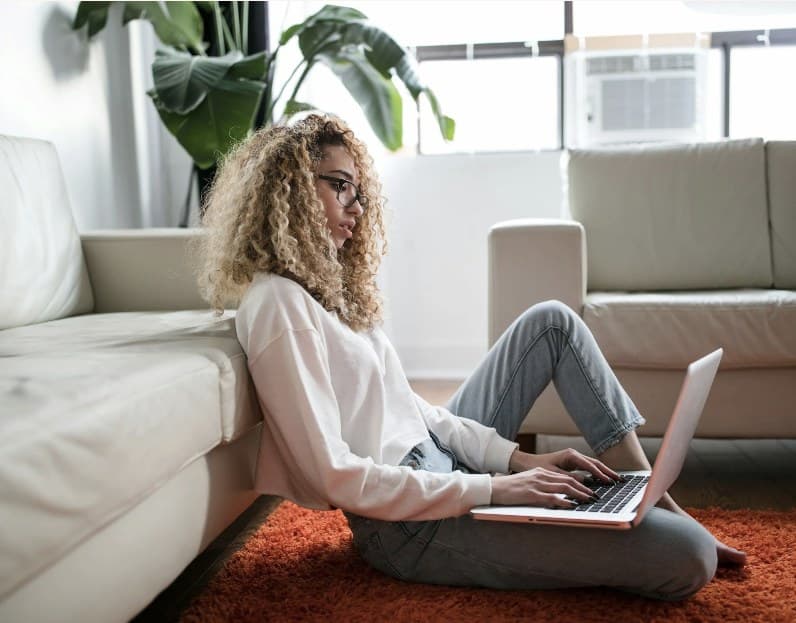 A woman sitting on the floor of her living room working on a laptop